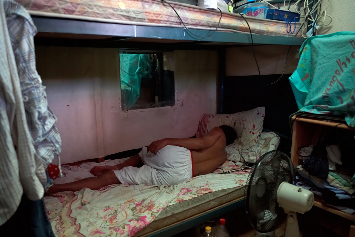Neisha 是一名二十五歲的印度人，來港五年。他正在自己狹窄的房間中睡覺。他居住的鍾屋村是十名難民的家園，但未來將要拆卸以興建洪水橋站。香港，2015年7月。